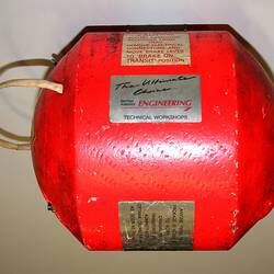Bright orange-red metal cylindrical casing with domed ends, plates and labels. Two cords fixed at ends.