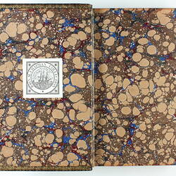 Open book with brown and beige marbled design on both sides. Printed label on left side with text and ship.