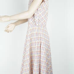 Knee length sleeveless dress with white, yellow, blue and red checked pattern, side view.