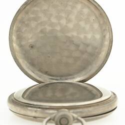 Silver metal round fob watch sitting within metal cover open to show inner side.