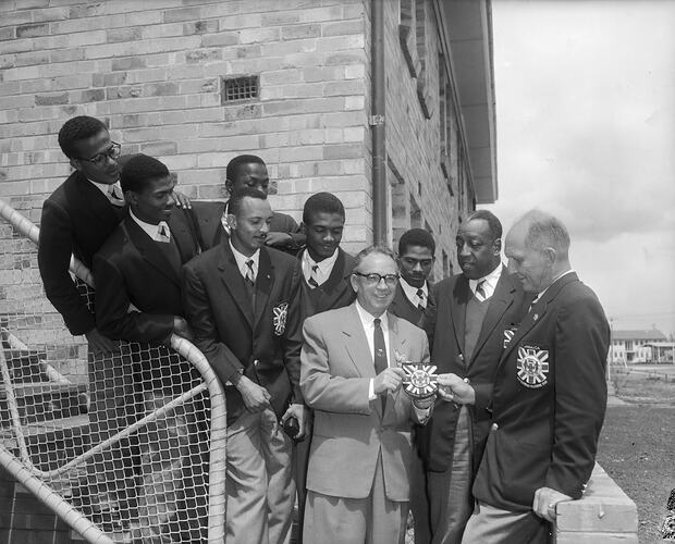 Man standing with sport team on staircase wearing sporting blazers.