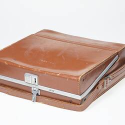 Tan leather carry case with leather hand strap and silver lock and trim. Gold lettering on outside.