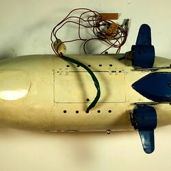 White model airship with blue nose, small wings. Lever and cables visible as underside view.