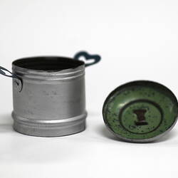 Side view of tiny aluminium pot and green underside of lid.