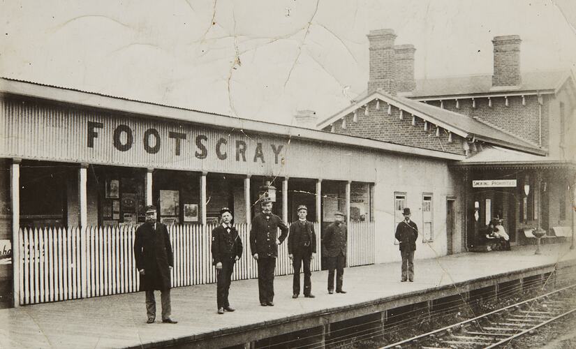 Six men in uniform standing on a platform at a railway station.