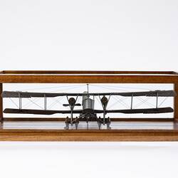Model of a bi-plane made mostly of aluminium sheet metal. It has two pairs of wheels at front. In display case