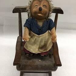 Hedgehog doll standing in wooden rocking chair.