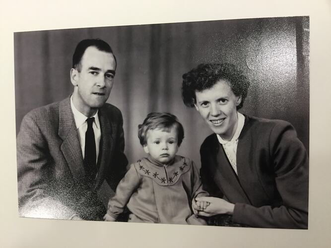 Man and woman pose either side of a toddler girl. Curtains behind.