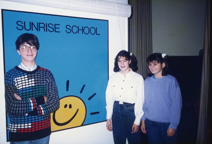 A group of young people standing in front of a blue sign that says 'Sunrise School'.