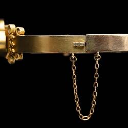 Detail of fine chain attached to gold bangle (bracelet) featuring a large gold nugget.