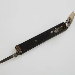 Quill pen cutter with black handle. Engraved silver metal quill cutter at one end, open knife at other end.