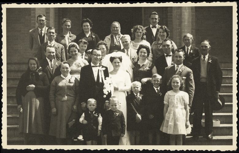 Group portrait of wedding party posing on steps. Bride and groom in centre near front.