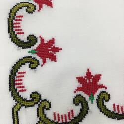 Detail of white cloth corner with green and red scalloped floral embroidery.