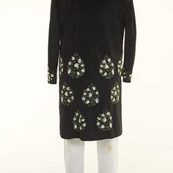 Black coat with white floral detail over white chinos pants. Back view.