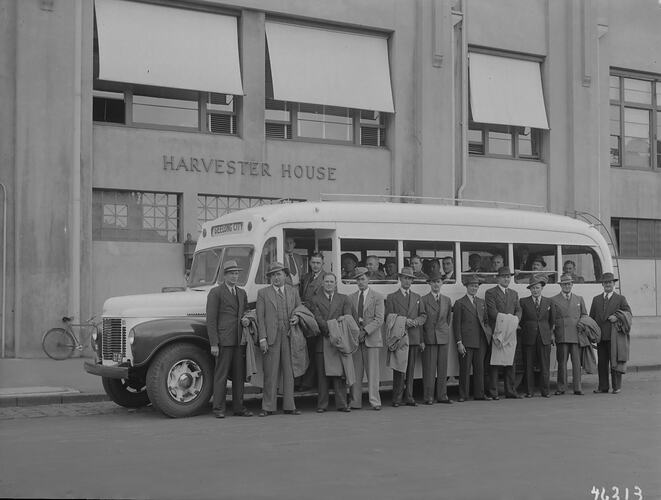 Men wearing suits and hats standing in front of a motor bus parked outside Harvester House.