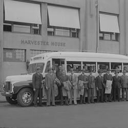 Men wearing suits and hats standing in front of a motor bus parked outside Harvester House.