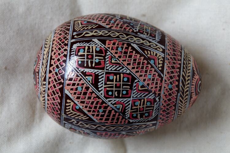 Egg, hand painted, intricate brown background with yellow, orange and white geometric design.