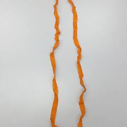 Rosette made from folded and looped bright orange ribbon. Pinned through centre, with a red white and blue ribbon.