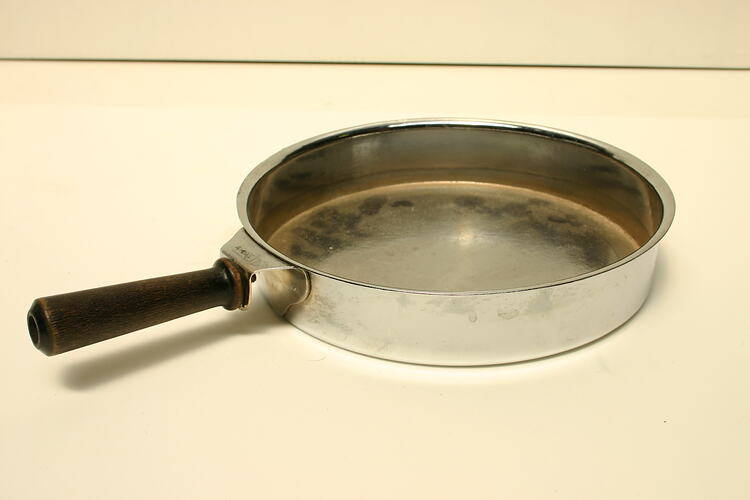 Shallow, circular pan with wooden bar handle.