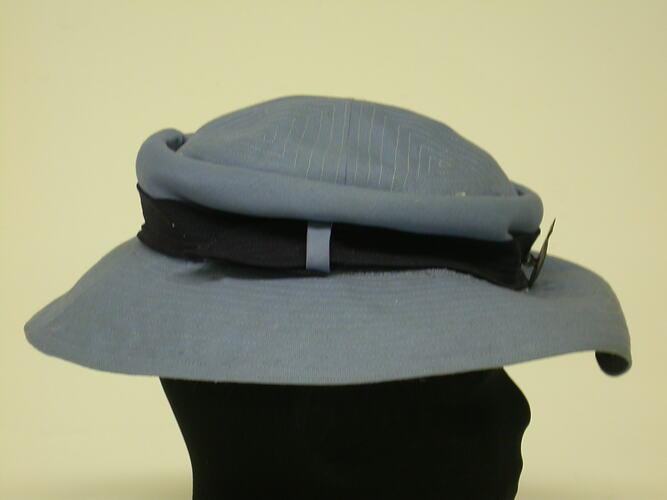 Blue hat with black hatband and metal broach, on black mannequin head, side view.