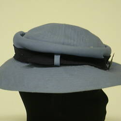 Blue hat with black hatband and metal broach, on black mannequin head, side view.