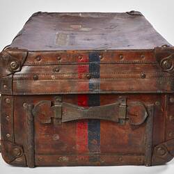 Side view of worn brown leather suitcase with handle. Faded red and black stripe.