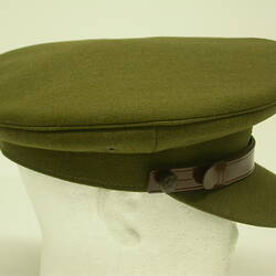 Green khaki cap with brown leather hat band on white mannequin head, side view.