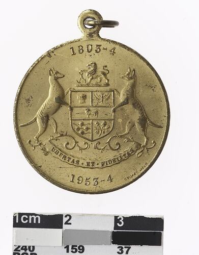 Round medal with Tasmanian coat of arms and text.
