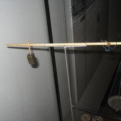 Ivory rod marked with lines. Rectagular brass weight hangs at one end and metal dish suspended from other end.