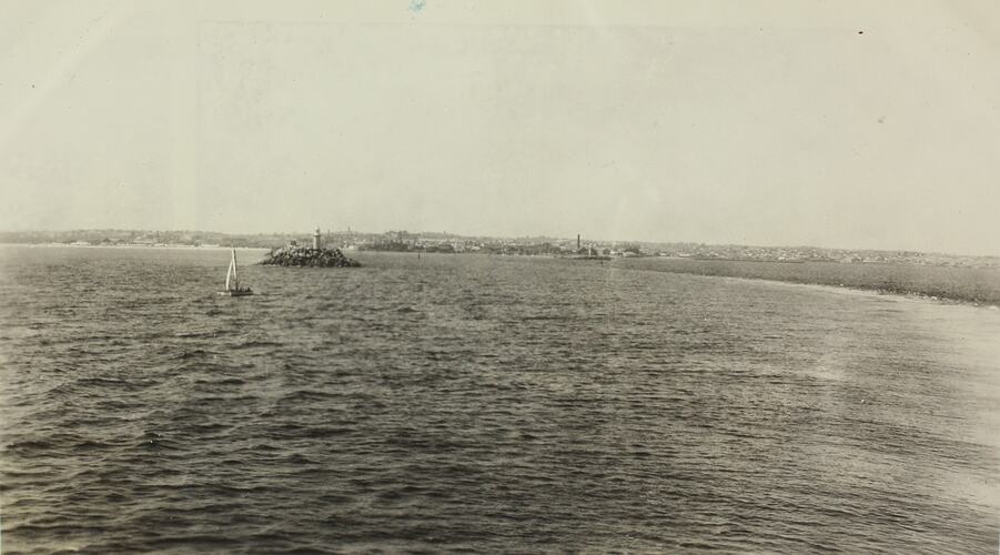 Seascape with a beacon on a rocky island and sail boat in the foreground. Second beacon in distance.