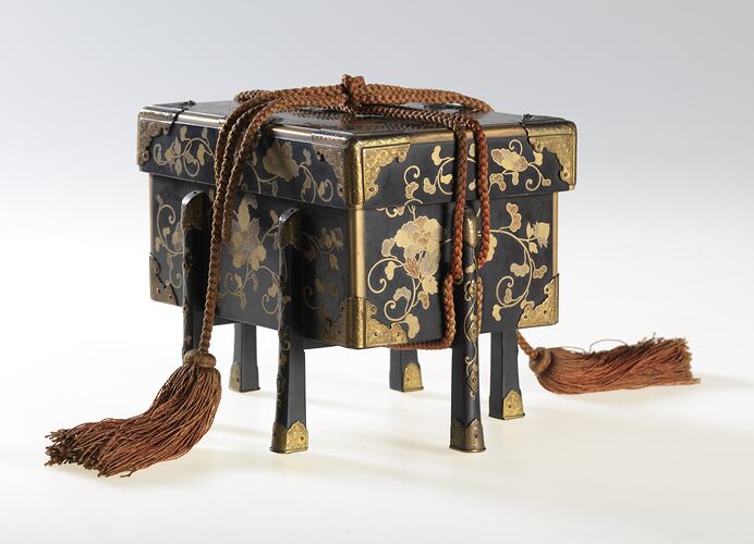 Lidded decorated, four-legged box tied with tassles.