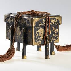 Lidded decorated, four-legged box tied with tassles.