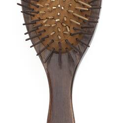 Wooden spoon-shaped hairbrush with long handle and rubber spikes attached via cushioning.