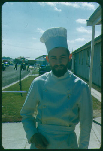 Man in chef's outfit standing outside a building.
