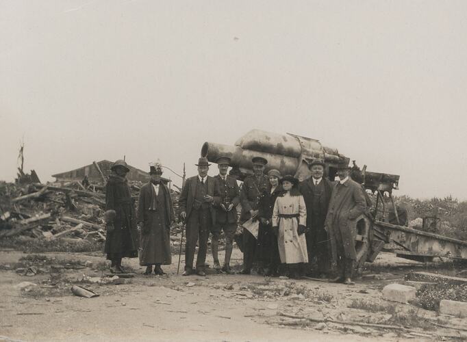 Group of men and women posing in front of a gun-howitzer.