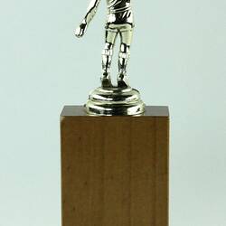 Trophy of golden basketballer on wooden stand. Back view.