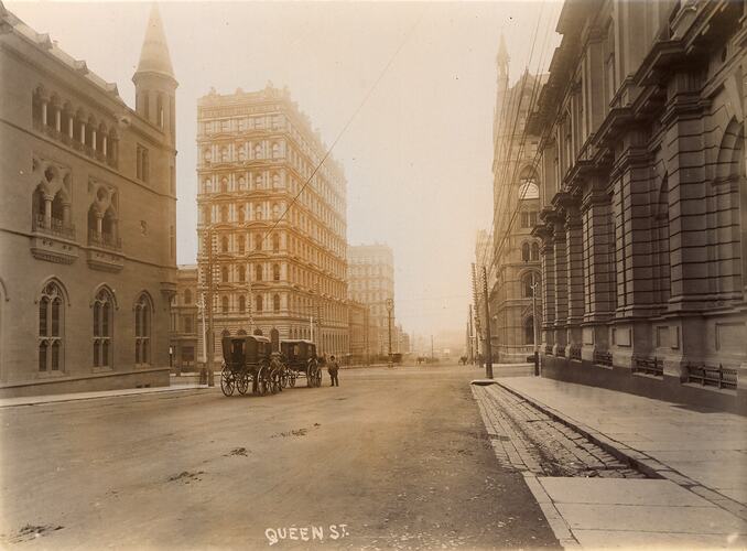 City street intersection showing multi-storied buildings. Horse drawn vehicles in street.