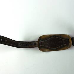 Brown leather bracelet with off-white stitching on edge with rounded copper plate threaded through straps.