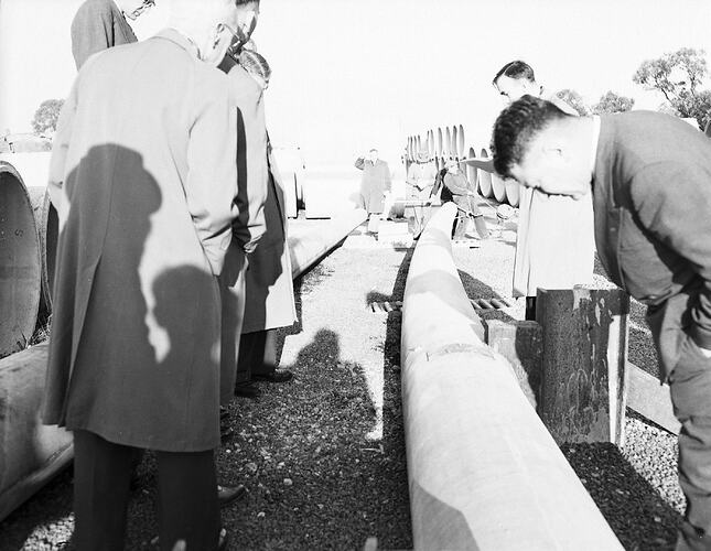Monochrome photograph of men testing cement pipes.