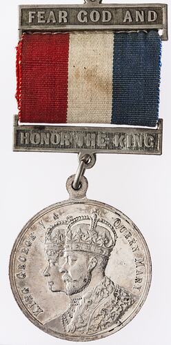 Round silver coloured medal with profile of crowned man and woman with text surrounding, and coloured ribbon.