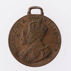 Round bronze medal with profile of man and woman's crowned heads facing left. Text above. Loop at top.