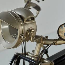 Motor cycle, head lamp and round registration badge detail.