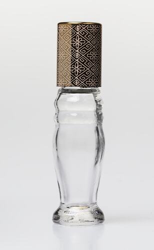 Curved glass perfume bottle, gold plastic lid. Lid has geometric design.