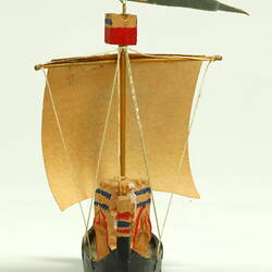 Rear view of ship with black hull and painted sail.