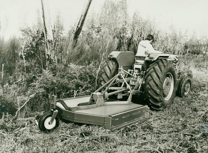 Man driving a tractor coupled to a rotary slasher through dense weeds and scrub.