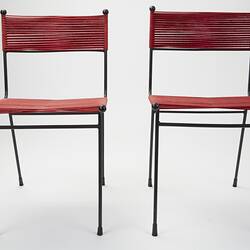 Two metal chairs strung with red cord seats and back sections. Front lower view.
