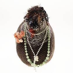 Hand-knitted brown chicken with pink rosettes and necklaces around its neck. Front view.