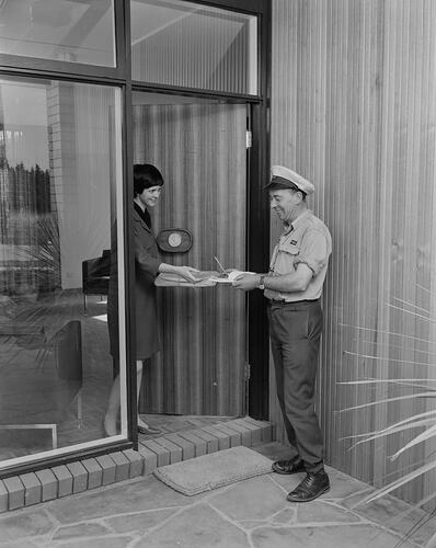 Woman taking delivery from post man. Gold medallion on door.