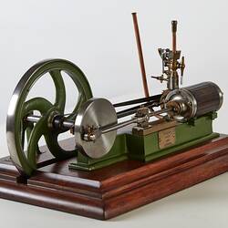 Metal model with large wheel and piston. Green painted frame, wooden base.