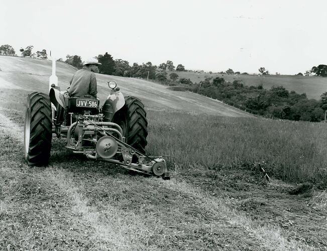 Rear view of man driving a tractor coupled with a mower.